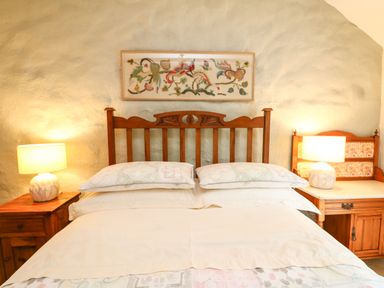 A bed with wooden headboard flanked by two bedside tables with lamps and a framed artwork above at Chenalls Cottage in Helston
