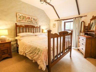 A bedroom with a wooden double bed bedside tables lamps a wooden dresser with a mirror and a window with curtains at Chenalls Cottage in Helston