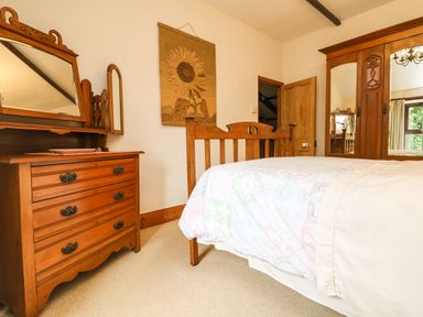 A bedroom with wooden furniture including a bed chest of drawers and wardrobe at Chenalls Cottage in Helston