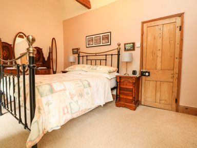 A bedroom with a metal bed frame a wooden dresser two lamps and a wooden door at Chenalls Cottage in Helston