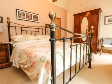 A bedroom with a metal bed frame a wooden wardrobe a wooden nightstand and a wicker chair at Chenalls Cottage in Helston