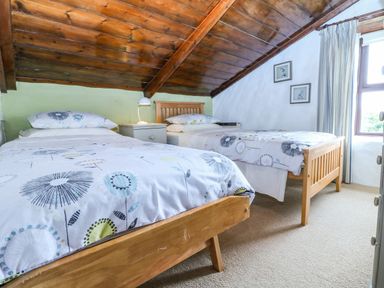 A bedroom with two single beds wooden ceiling and a window with curtains at Chenalls Cottage in Helston
