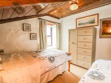 A bedroom with two beds a wooden dresser and framed pictures on the wall at Chenalls Cottage in Helston