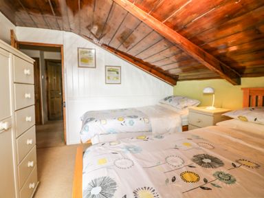 A bedroom with two single beds a chest of drawers and a bedside table with a lamp at Chenalls Cottage in Helston
