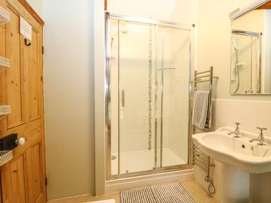 A bathroom with a glass shower enclosure pedestal sink wooden door and towel radiator at Chenalls Cottage in Helston