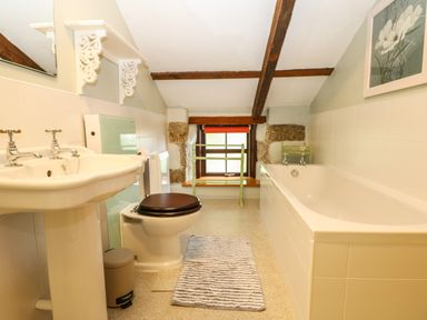 A bathroom with a bathtub a toilet a sink a window with wooden trim and a drying rack at Chenalls Cottage in Helston