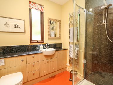 A bathroom with wooden cabinets a white sink a glass shower enclosure and a towel rack at Chenalls Cottage in Helston