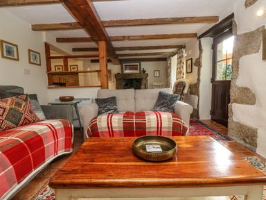 A living room with wooden beams on the ceiling sofas with plaid blankets and a wooden coffee table with a metallic bowl at Chenalls Cottage in Helston