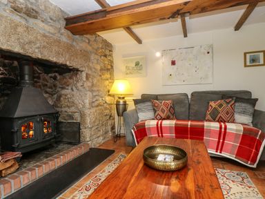 A living room with a wood stove fireplace a sofa with patterned cushions a red plaid throw and a wooden coffee table at Chenalls Cottage in Helston