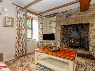 A living room with a wooden coffee table a wood burning stove and a television at Chenalls Cottage Helston