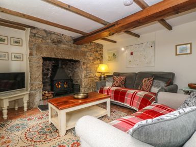 A living room with a stone fireplace sofas with red plaid throws a wooden coffee table and a television at Chenalls Cottage in Helston