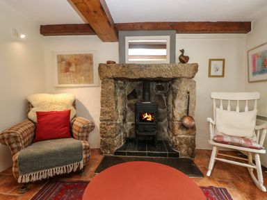 A sitting room with a stone fireplace wood stove armchair and rocking chair at Chenalls Cottage in Helston