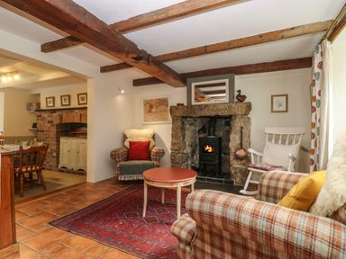 A living room with a wood stove fireplace wooden beams and plaid armchairs at Chenalls Cottage in Helston