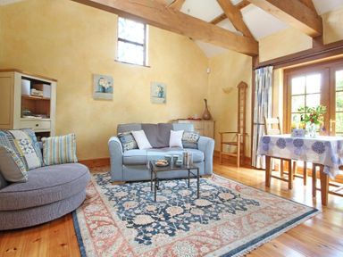 A living room with sofas a coffee table a rug wooden beams and a dining table at Summer House in Helston