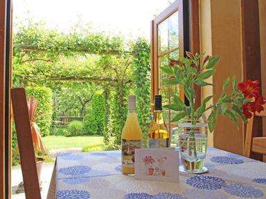 A table with two bottles flowers and a card near an open door showing a garden at Summer House in Helston