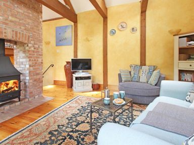 A living room with a wood burning stove a patterned rug a television on a stand and two sofas at Summer House in Helston