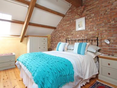 A bedroom with a bed with turquoise throw and pillows a brick wall wooden beams and furniture at Summer House in Helston