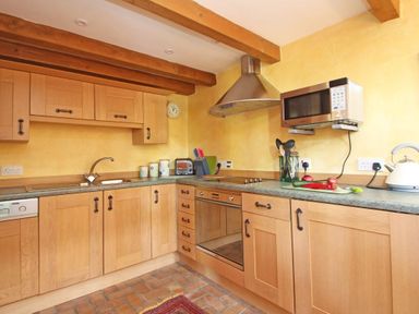 A kitchen with wooden cabinets, a built-in oven, a microwave, a toaster, utensils in a jar, and a kettle on a countertop at Summer House in Helston
