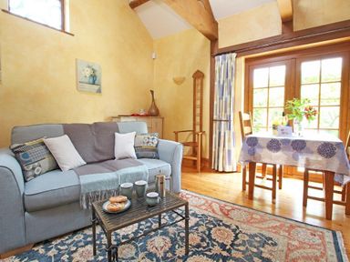 A living room with a sofa table with cups and pastries and a dining table by window at Summer House in Helston