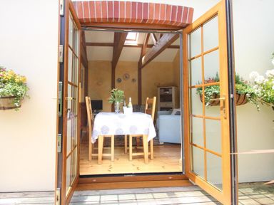 A dining area with a table and chairs viewed through open wooden double doors at Summer House in Helston