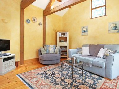 A living room with a blue sofa a round gray chair a small metal coffee table a patterned rug a wooden cabinet and a television at Summer House in Helston