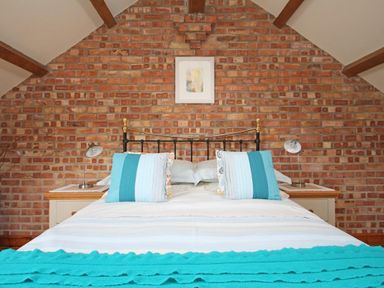 A bedroom with a bed against a brick wall and two bedside tables with lamps at Summer House in Helston