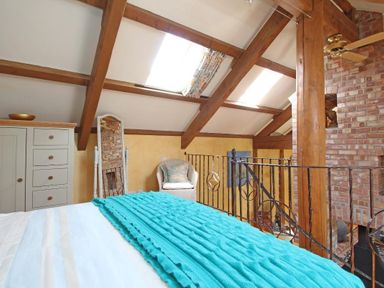 A bedroom with wooden beams a white dresser a full-length mirror and a wicker chair at Summer House in Helston