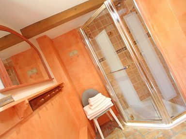 A bathroom with a glass shower enclosure a chair with folded towels wooden beams and a mirror at Summer House in Helston