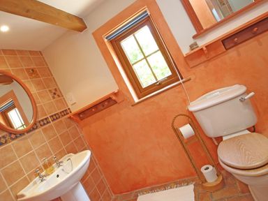 A bathroom with a toilet a sink a circular mirror a window and a toilet paper holder at Summer House in Helston