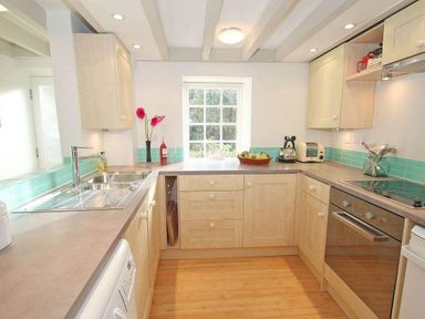 A kitchen with wooden cabinets a sink an oven and a window at White Duck Cottage in Hayle