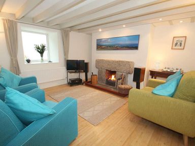 A living room with blue and green chairs a fireplace and a television at White Duck Cottage in Hayle