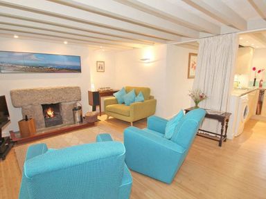A living room with two blue armchairs and one yellow armchair by a stone fireplace at White Duck Cottage in Hayle