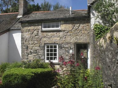 A stone cottage with two windows and a door surrounded by plants and flowers at White Duck Cottage in Hayle