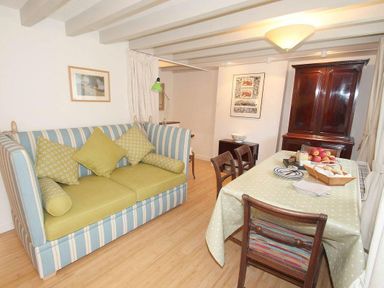 A room with a striped sofa and yellow cushions a dining table with chairs and fruit bowls and a wooden cabinet at White Duck Cottage in Hayle