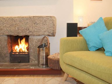 A stone fireplace with a fire burning next to a green sofa with blue cushions at White Duck Cottage in Hayle
