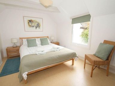 A bedroom with a double bed two bedside tables with lamps a window and a wicker chair at White Duck Cottage in Hayle