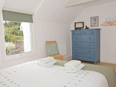 A bedroom with a bed with folded towels blue chest of drawers and a window at White Duck Cottage in Hayle