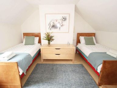 A bedroom with two single beds a dresser with flowers and a framed picture at White Duck Cottage in Hayle