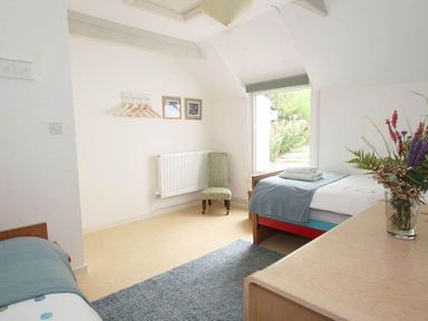 A bedroom with two single beds a green chair a window and flowers on a dresser at White Duck Cottage in Hayle
