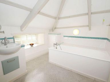 A bathroom with a bathtub sink window and exposed beams at White Duck Cottage in Hayle