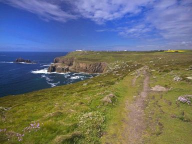 A coastal path overlooking cliffs and the ocean under a partly cloudy sky at White Duck Cottage in Hayle