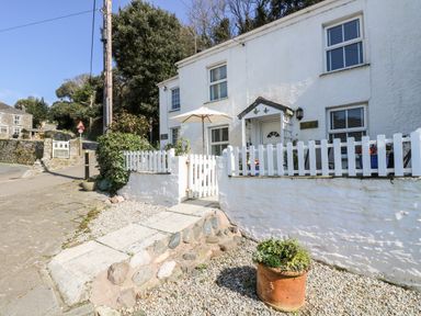A white house with a white picket fence and stone pathway with potted plants outside at Mallards in Pentewan