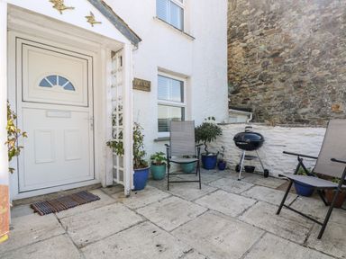 A small outdoor patio area with two chairs a barbecue grill plants in pots and a white door at Mallards in Pentewan