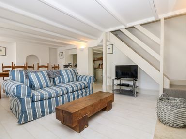 A living room with a striped sofa wooden coffee table TV under stairs and dining table at Mallards in Pentewan