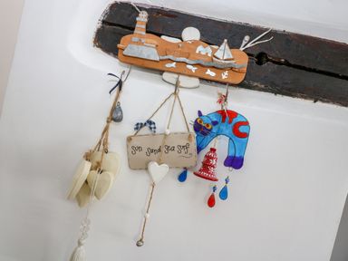Decorative hanging ornaments including wooden hearts a sign saying sun sand sea surf and a colorful cat hanging on hooks mounted on a wall at Mallards in Pentewan