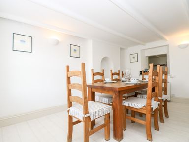 A dining room with a wooden table surrounded by six wooden chairs with striped cushions at Mallards in Pentewan