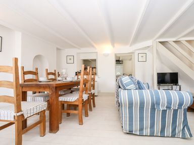 A dining area with wooden chairs and a table next to a living space with a striped blue and white sofa and a television at Mallards in Pentewan
