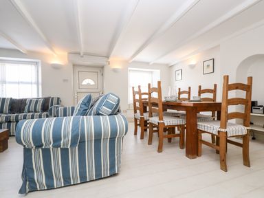 A dining area with a wooden table and six chairs next to a living area with blue and white striped sofas at Mallards in Pentewan