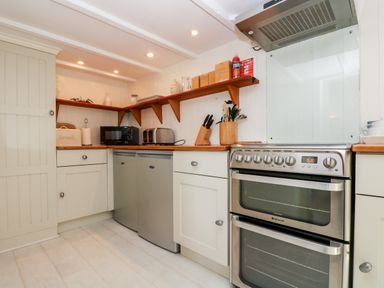 A kitchen corner with a stainless steel oven fridge microwave toaster and wooden shelves at Mallards in Pentewan