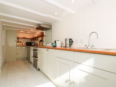 A kitchen with white cabinets wooden countertops a stove microwave kettle and sink at Mallards in Pentewan
